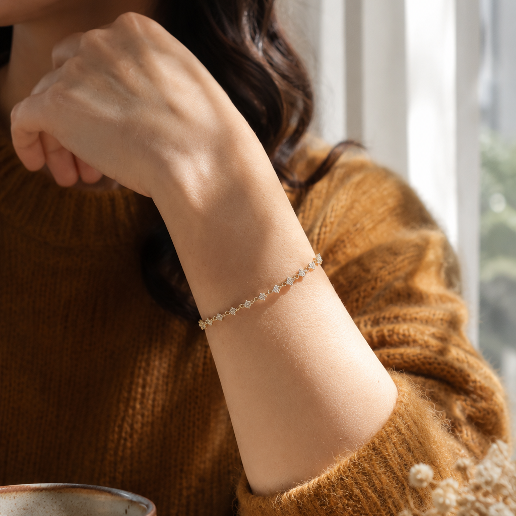 Close-up lifestyle photo of an elegant 18K gold flower chain bracelet worn on a woman's wrist beside a ceramic coffee cup in warm natural morning sunlight, showcasing delicate everyday luxury jewelry.