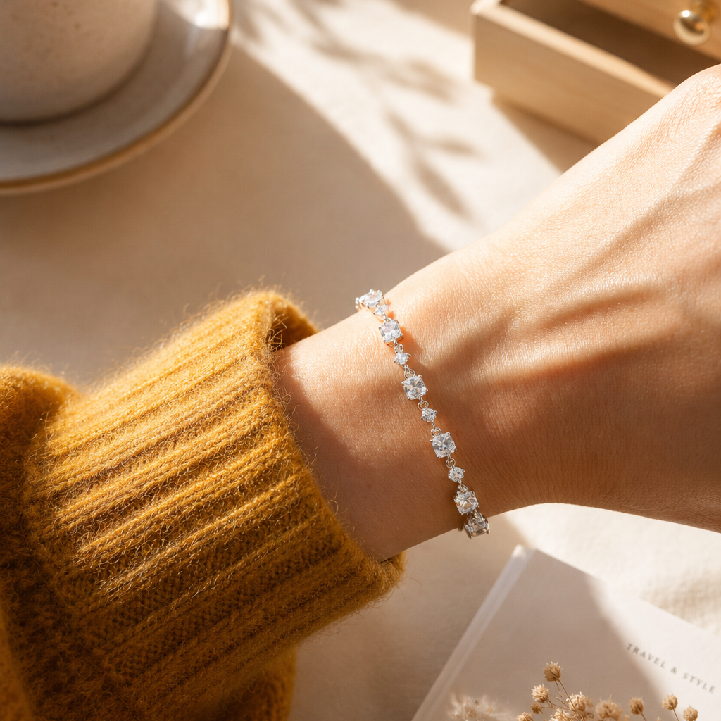 Close-up lifestyle photo of a 925 sterling silver cubic zirconia tennis bracelet on a woman's wrist, illuminated by warm natural sunlight beside a coffee cup and jewelry box, creating an elegant everyday luxury look.