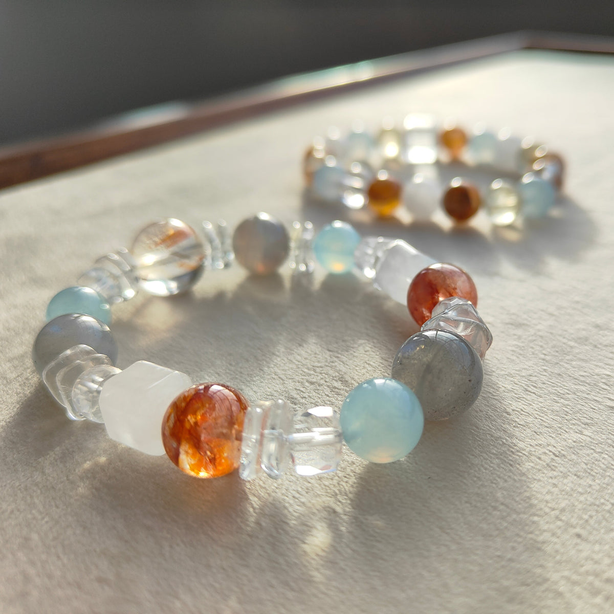 Handmade beaded stretch bracelets with translucent and colourful gemstone beads displayed in warm natural sunlight on a textured neutral surface.