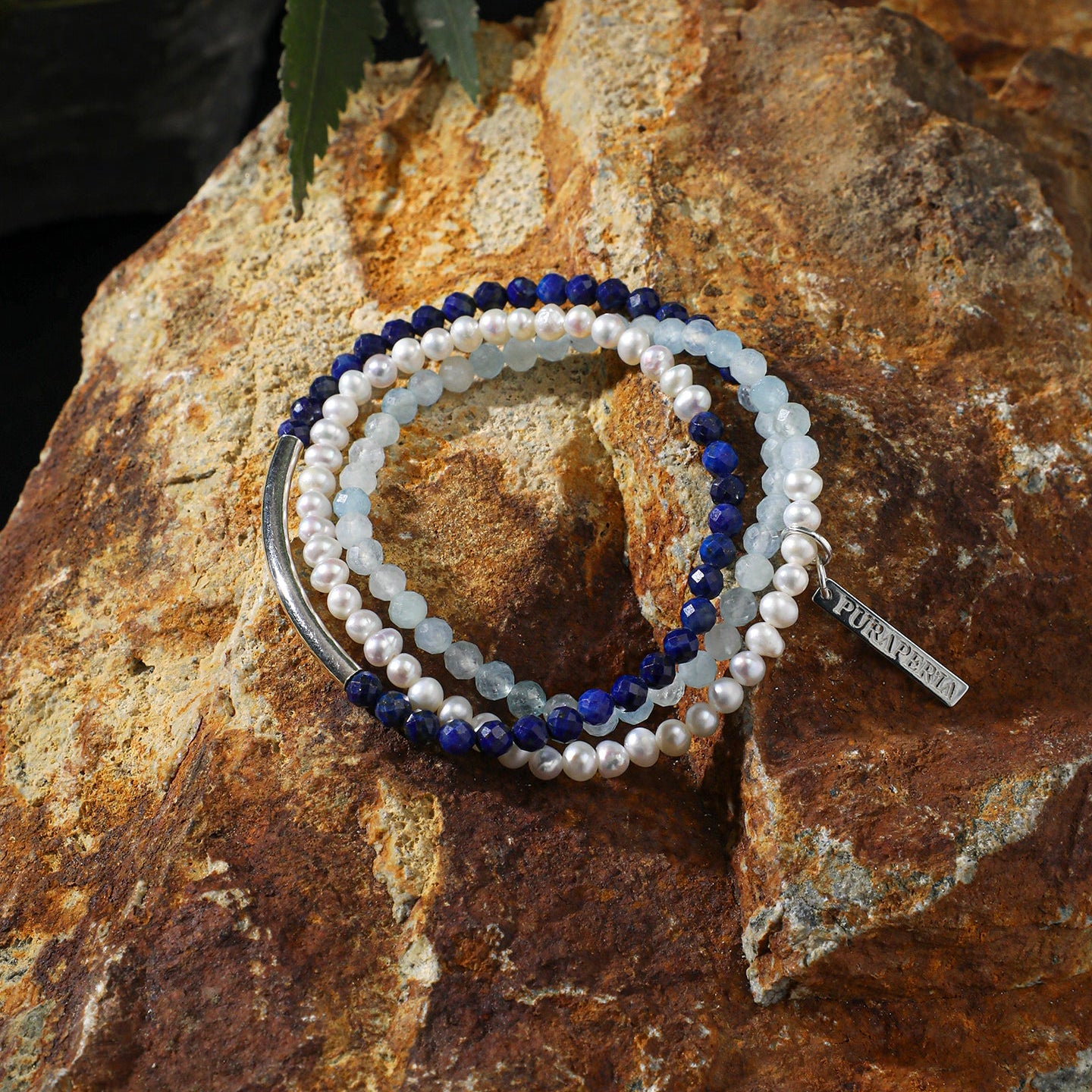 Aquamarine, lapis lazuli and freshwater pearl layered bracelet displayed on natural rock