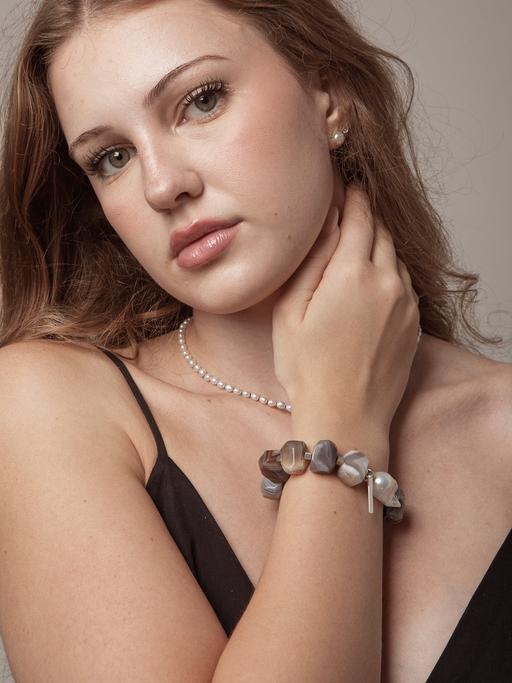 Woman wearing a pearl necklace and bracelet against a neutral background
