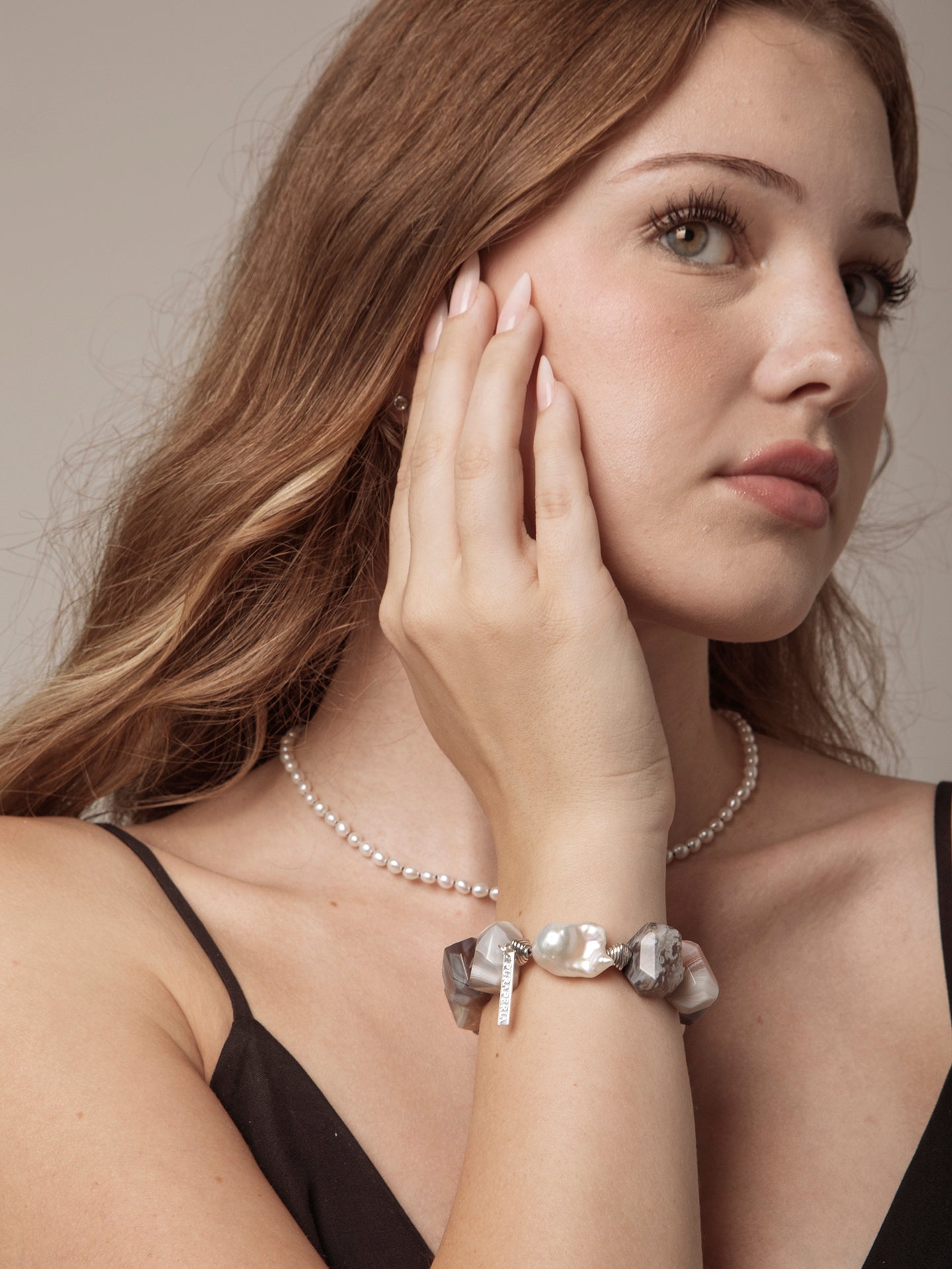 Woman wearing a pearl necklace and bracelet against a neutral background