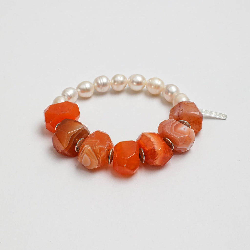 Angled view of handcrafted carnelian and freshwater pearl statement bracelet with silver-tone accents