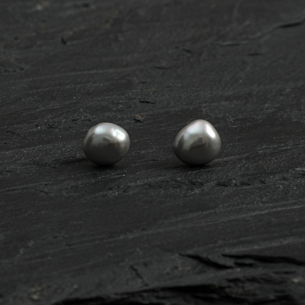 Front view of grey baroque freshwater pearl stud earrings on a dark natural surface