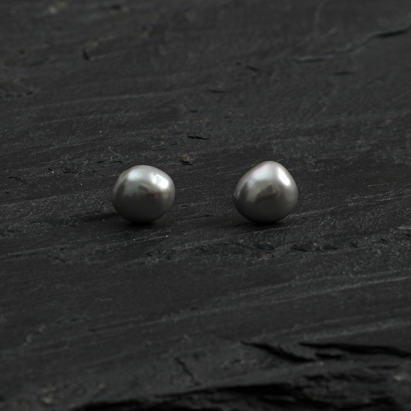Front view of grey baroque freshwater pearl stud earrings on a dark natural surface