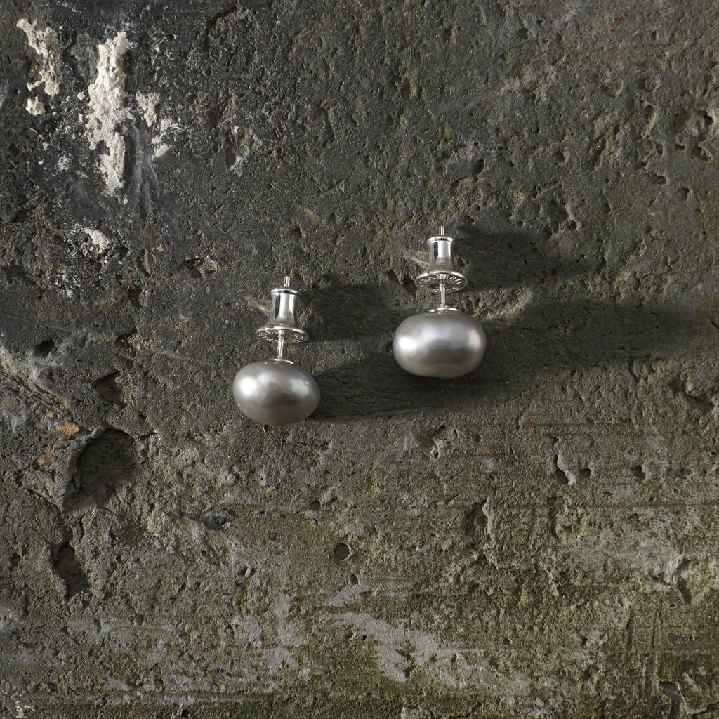 Grey baroque freshwater pearl stud earrings styled on a dark natural stone surface