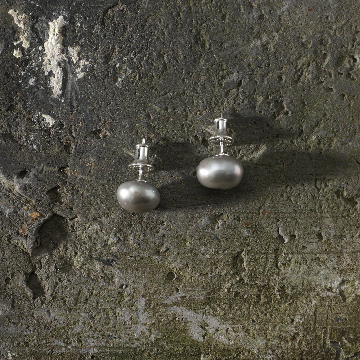 Grey baroque freshwater pearl stud earrings styled on a dark natural stone surface