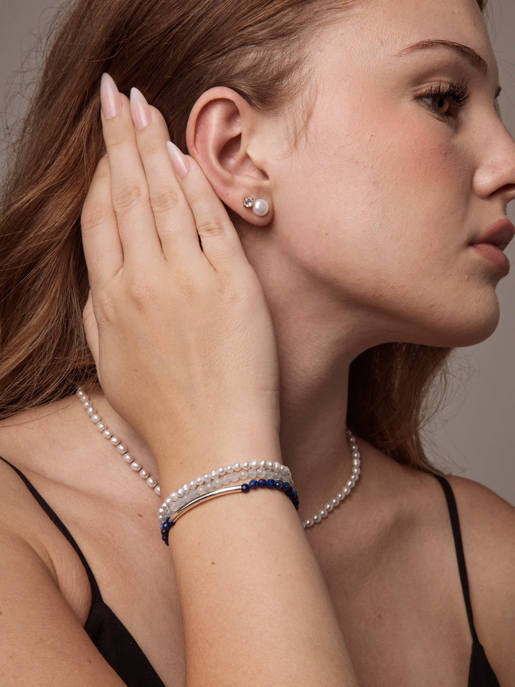 Close-up of a woman wearing a handcrafted lapis lazuli and freshwater pearl bracelet with matching pearl stud earrings and a pearl necklace, showcasing timeless handcrafted jewellery by Puro Craft.
