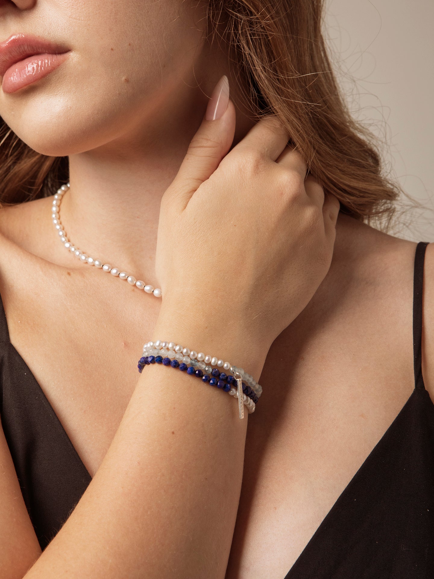 Woman wearing layered handmade lapis lazuli and freshwater pearl bracelets with a pearl necklace, showcasing elegant handcrafted jewellery by Puro Craft.