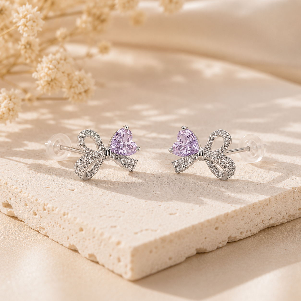 Lavender Ice-Cut CZ Bow stud earrings in rhodium-plated 925 sterling silver displayed on a warm neutral stone surface