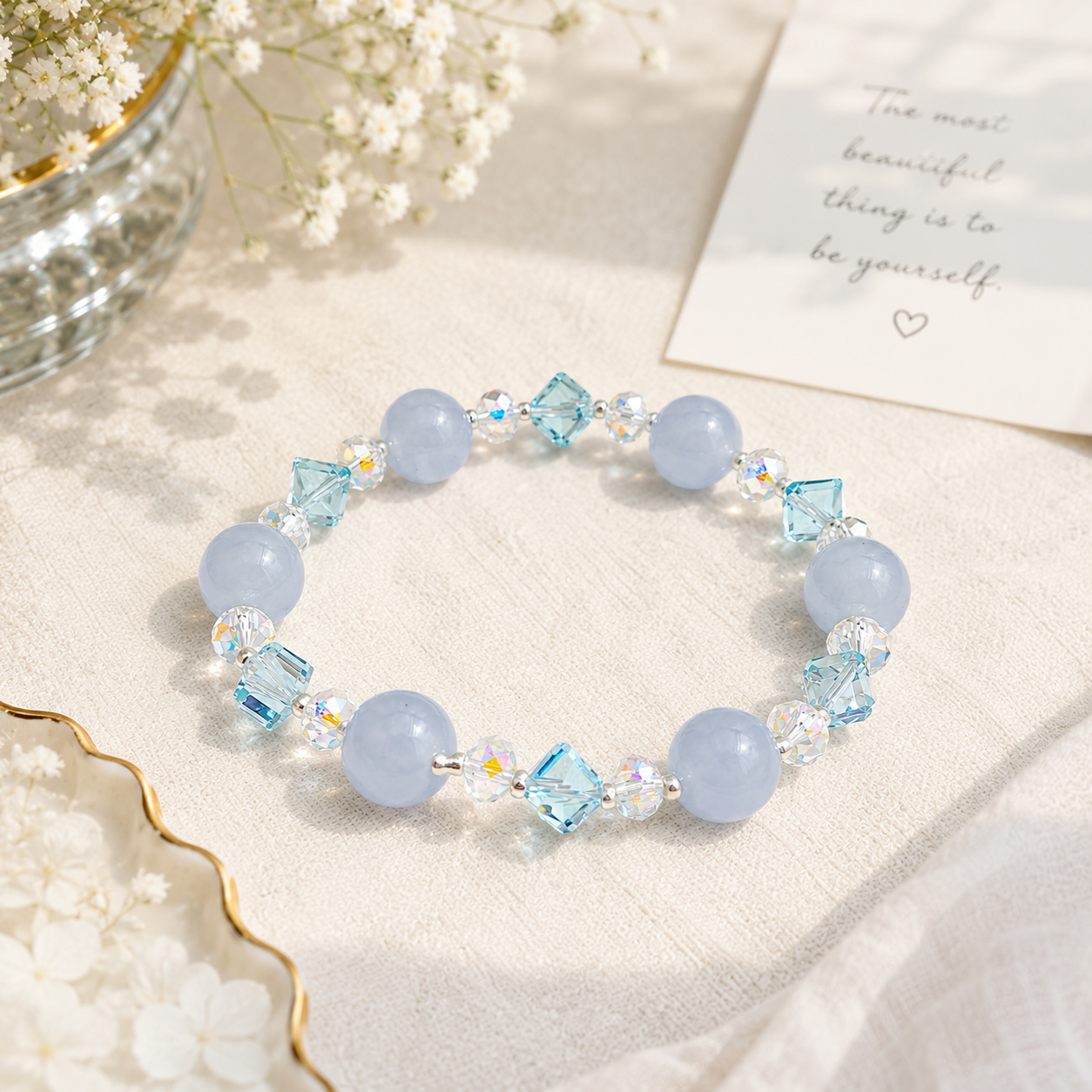 Lifestyle image of a handmade bracelet featuring 10mm natural aquamarine beads, 5mm blue faceted crystal cube beads, 6mm aurora crystal accent beads and silver-tone spacer beads, displayed on a soft linen surface in natural light.
