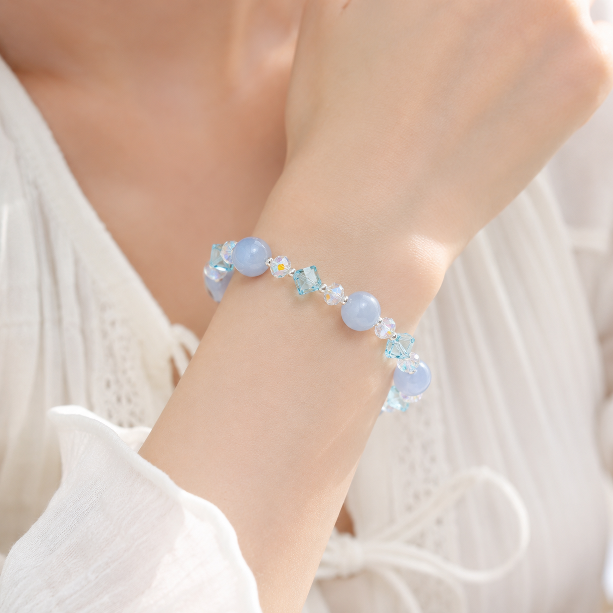 Close-up of a woman wearing a handmade bracelet featuring 10mm natural aquamarine beads, 5mm blue faceted crystal cube beads, 6mm aurora crystal accent beads and silver-tone spacer beads.