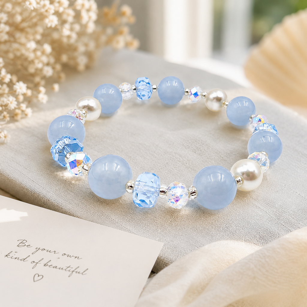 Lifestyle image of a handmade bracelet featuring 10mm natural aquamarine beads, 8mm genuine freshwater pearls, 8mm blue faceted crystal beads, 6mm aurora crystal accent beads and silver-tone spacer beads, displayed on a soft linen surface in natural light.