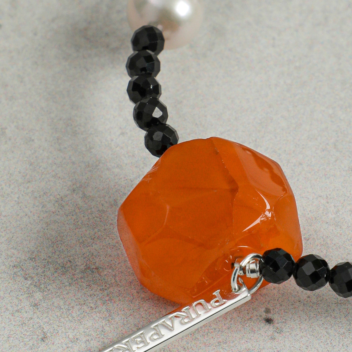 Close-up detail of a handcrafted natural carnelian, faceted black onyx and freshwater pearl bracelet, highlighting the rich orange carnelian focal stone and artisan craftsmanship.