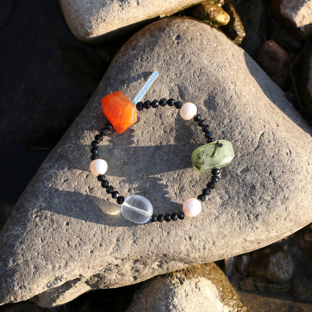 Handcrafted natural carnelian, prehnite, clear quartz, black onyx and freshwater pearl bracelet displayed on a sunlit natural stone, showcasing genuine gemstones, organic textures and artisan craftsmanship.