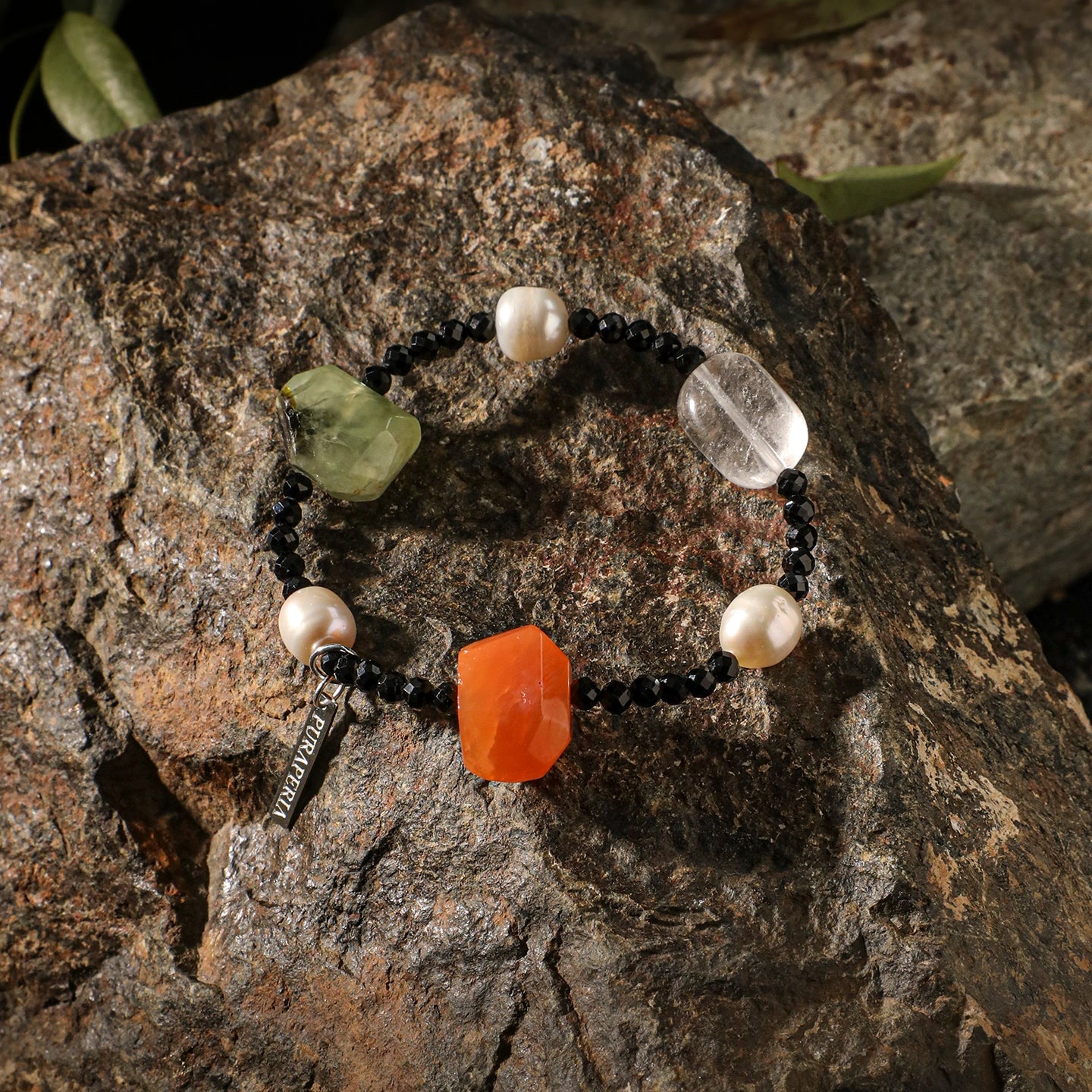 Handcrafted natural carnelian, prehnite, clear quartz, black onyx and freshwater pearl bracelet displayed on a natural rock surface, highlighting the unique gemstones and artisanal craftsmanship in warm natural light.