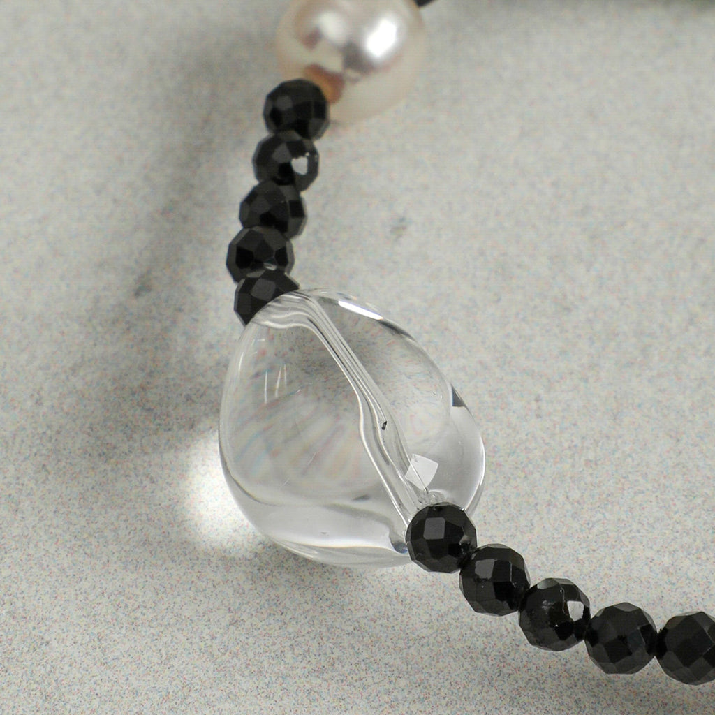 Close-up detail of a handcrafted natural clear quartz, faceted black onyx and freshwater pearl necklace, highlighting the polished clear quartz focal bead and elegant gemstone craftsmanship.