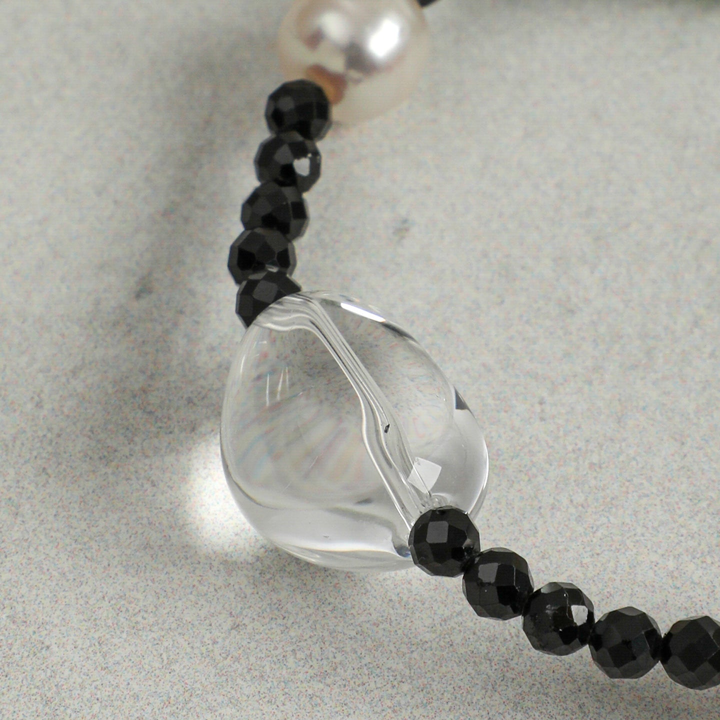 Close-up detail of a handcrafted natural clear quartz, faceted black onyx and freshwater pearl necklace, highlighting the polished clear quartz focal bead and elegant gemstone craftsmanship.