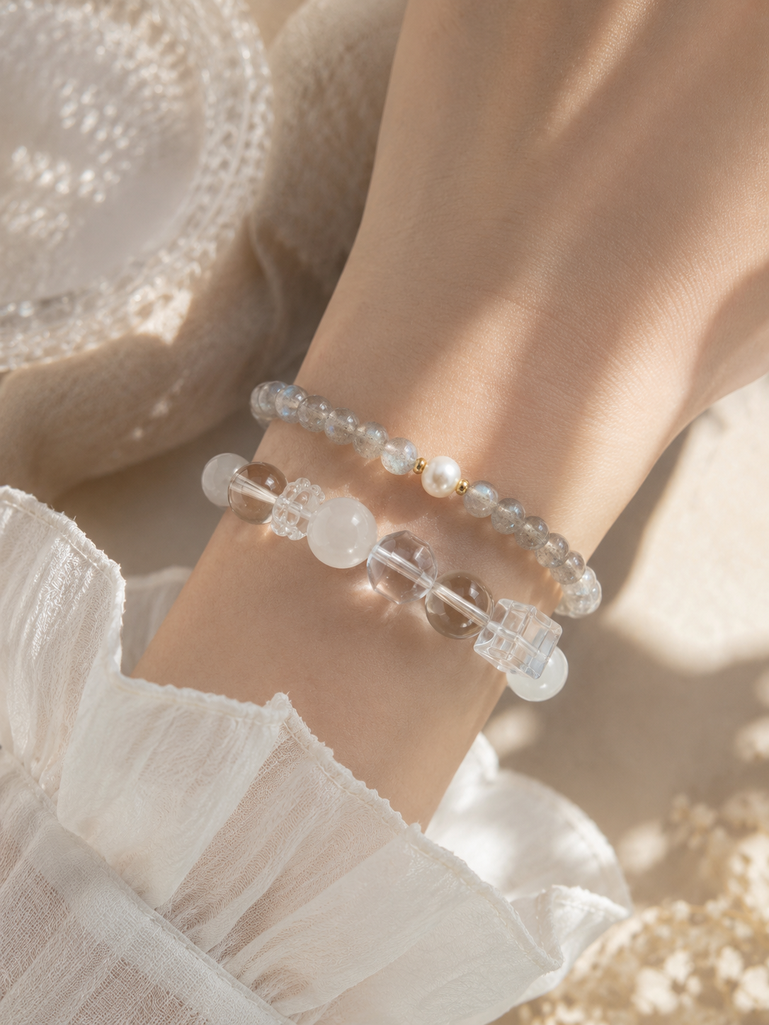 Woman wearing a handmade natural grey moonstone bracelet featuring 4mm grey moonstone beads, a 6mm genuine freshwater pearl and gold-tone spacer beads, styled with a clear quartz and white jade beaded bracelet.