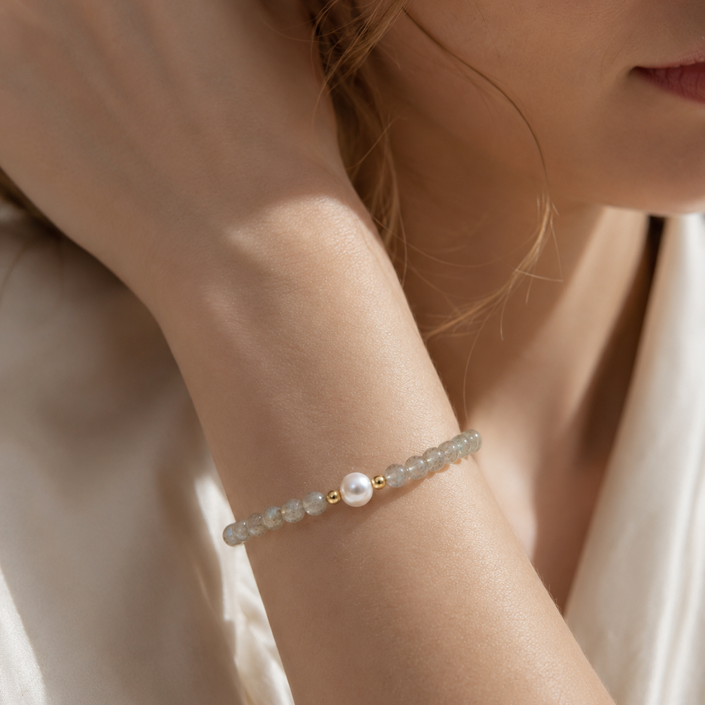 Close-up of a woman wearing a handmade natural grey moonstone bracelet featuring 4mm grey moonstone beads, a 6mm genuine freshwater pearl and gold-tone spacer beads in soft natural light.