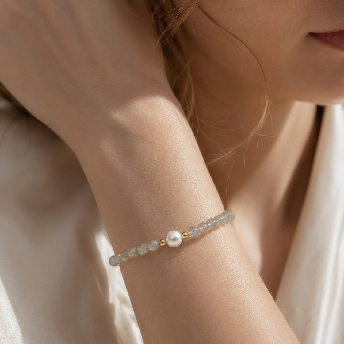 Close-up of a woman wearing a handmade natural grey moonstone bracelet featuring 4mm grey moonstone beads, a 6mm genuine freshwater pearl and gold-tone spacer beads in soft natural light.