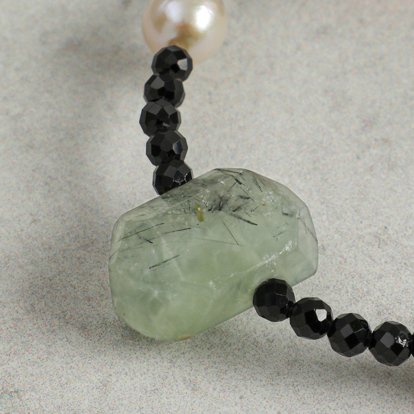 Close-up detail of a handcrafted natural prehnite, faceted black onyx and freshwater pearl necklace, highlighting the unique texture, natural inclusions, and artisan craftsmanship of the prehnite focal stone.