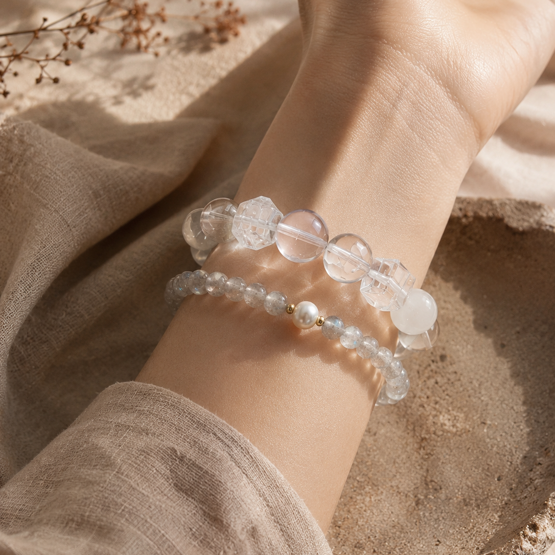 Woman wearing a handmade natural white phantom quartz and clear quartz bracelet featuring 10mm white phantom quartz beads, 10mm clear quartz beads, 10mm faceted clear quartz cube beads and a clear floral spacer bead, styled with a grey moonstone and freshwater pearl bracelet.
