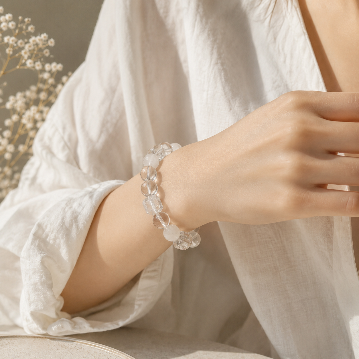 Close-up of a woman wearing a handmade bracelet featuring 10mm natural white phantom quartz beads, 10mm clear quartz beads, 10mm faceted clear quartz cube beads and a clear floral spacer bead.