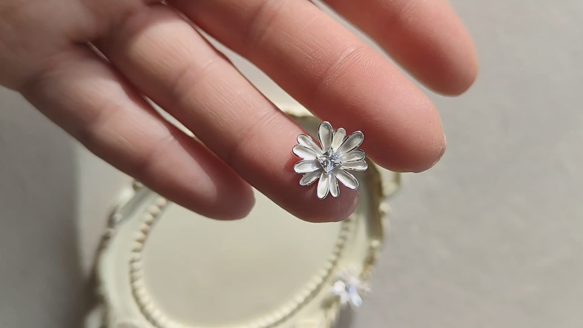 Close-up of a flower-shaped silver stud earring with a sparkling CZ centre held between fingers in natural light.