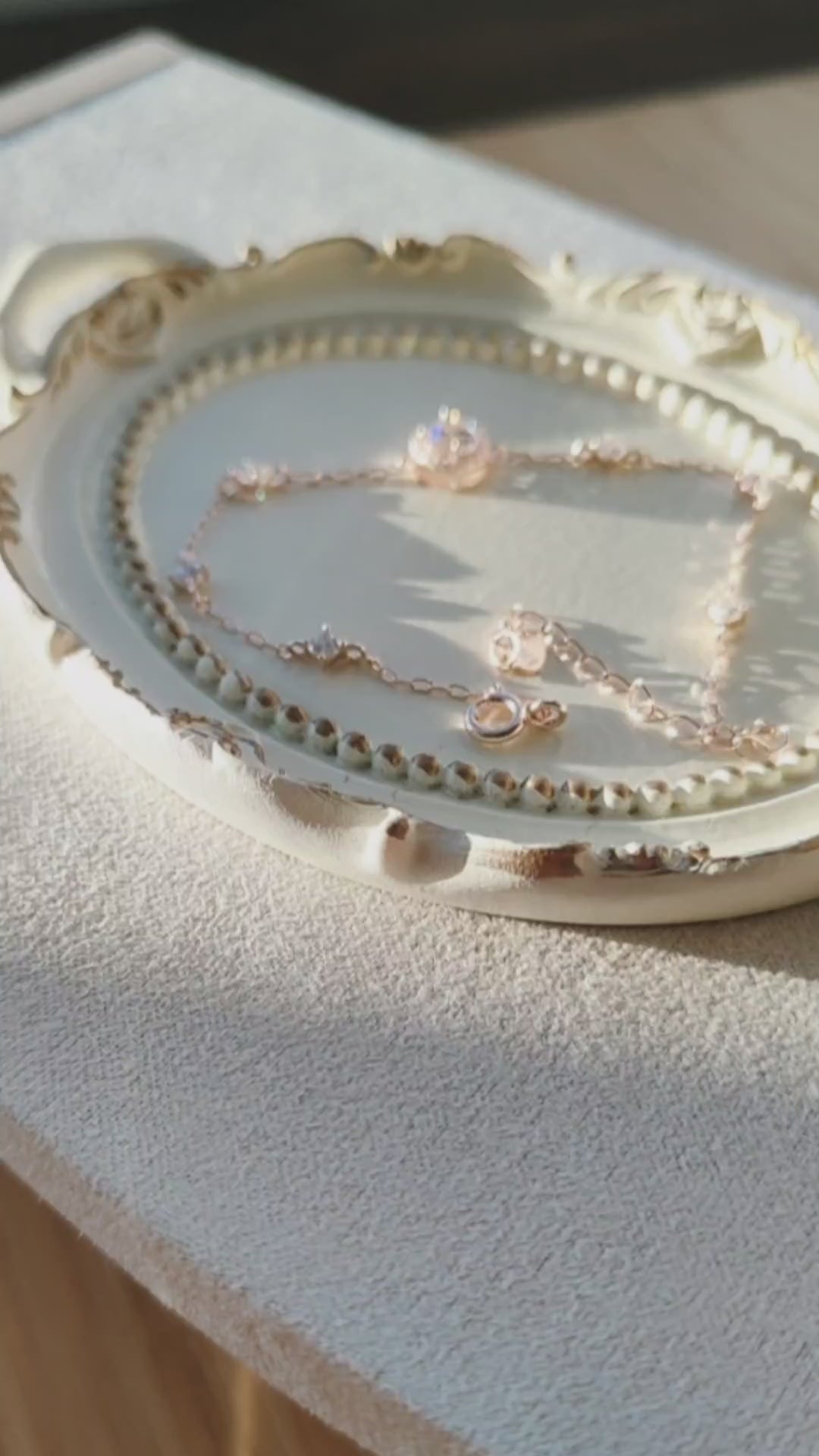 Delicate rose gold necklace with sparkling CZ details arranged on a decorative jewellery tray in warm natural sunlight.