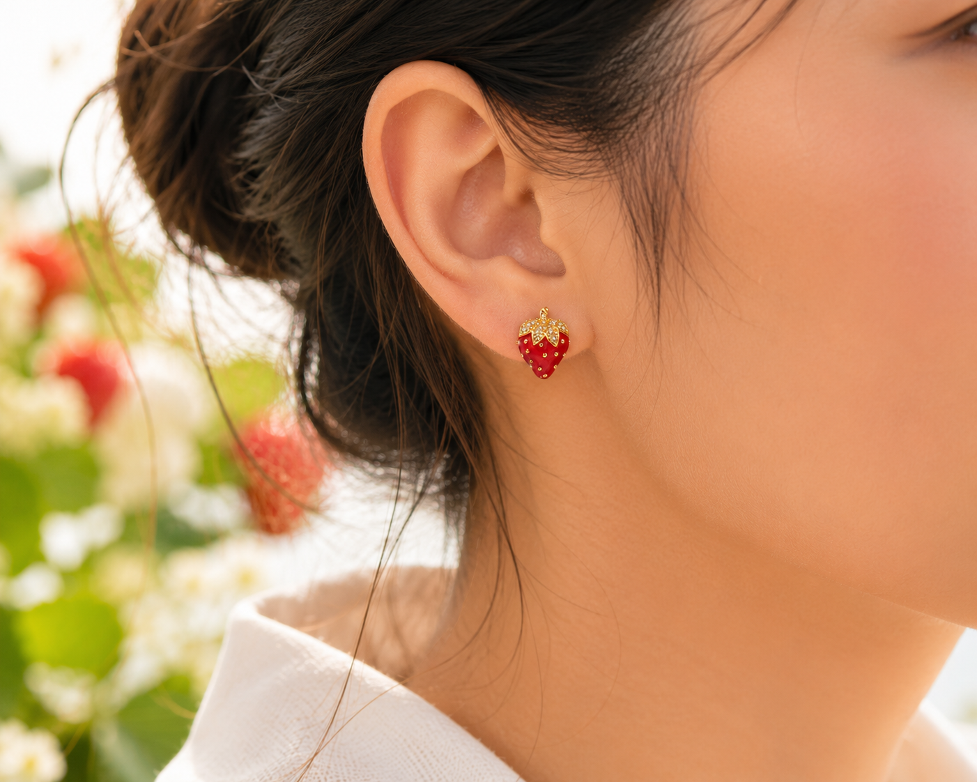 Red strawberry gold-tone stud earring with sparkling accents worn on right ear