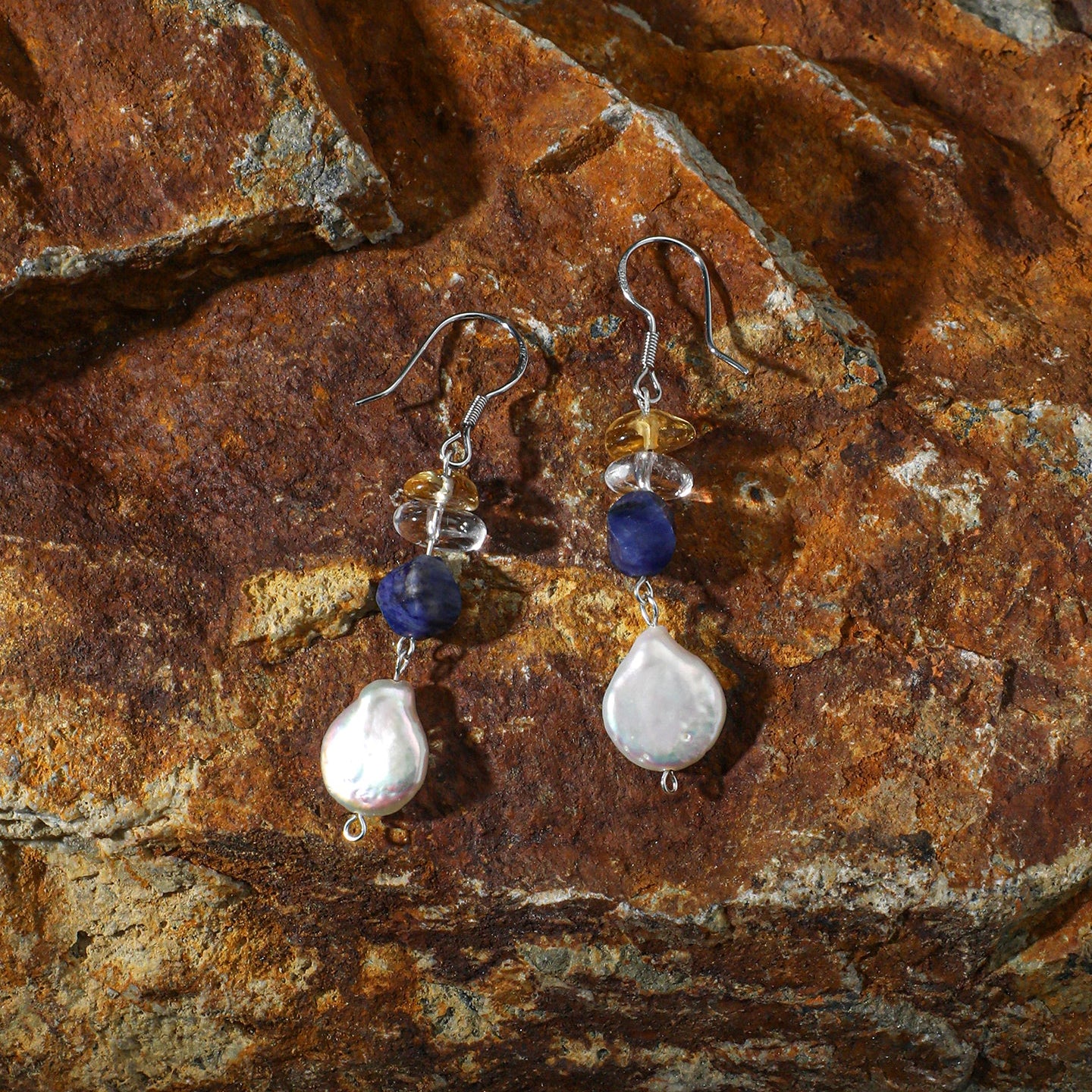 Sodalite, citrine and freshwater pearl drop earrings styled on natural rock