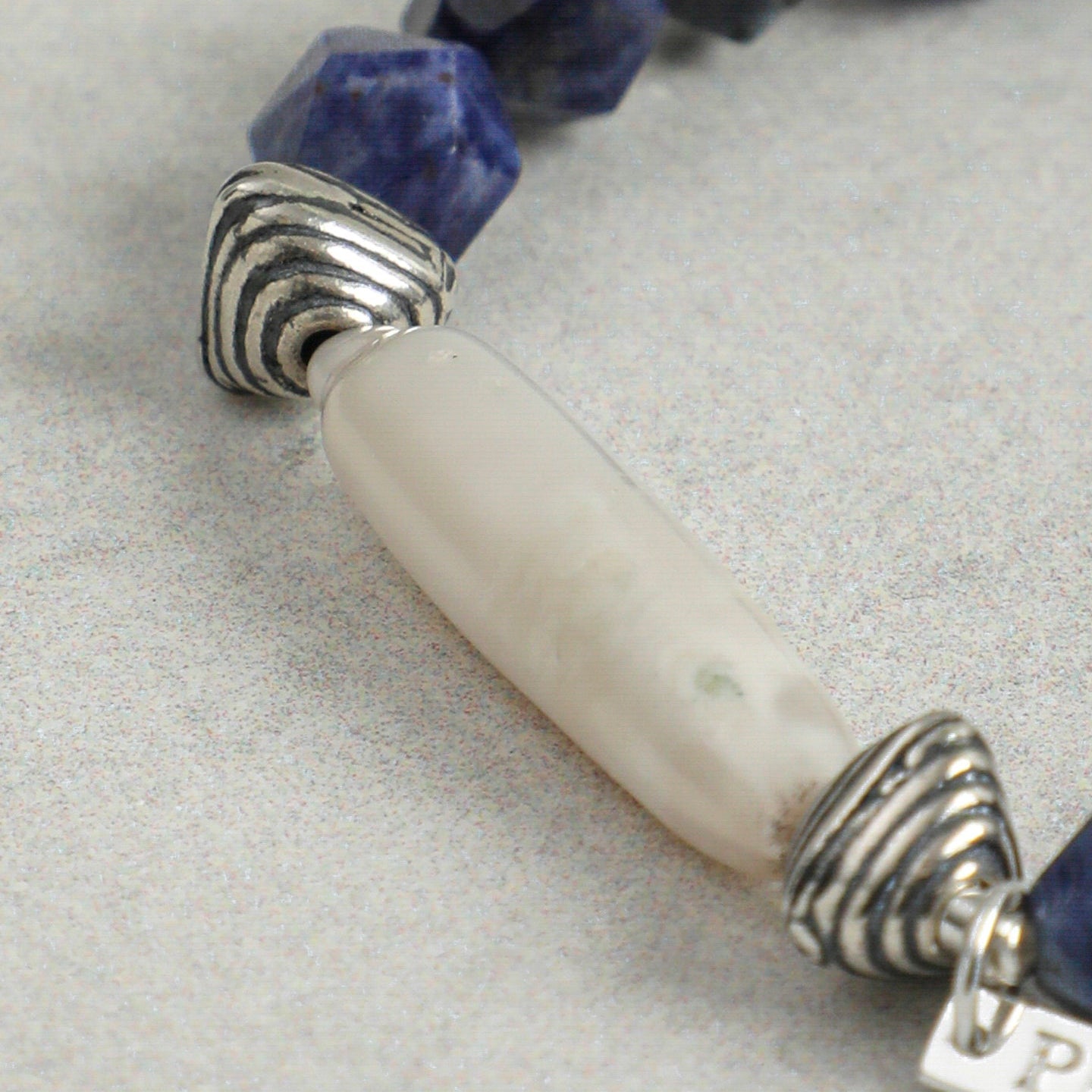 Close-up of elongated freshwater pearl with textured silver-tone accents and faceted sodalite gemstones