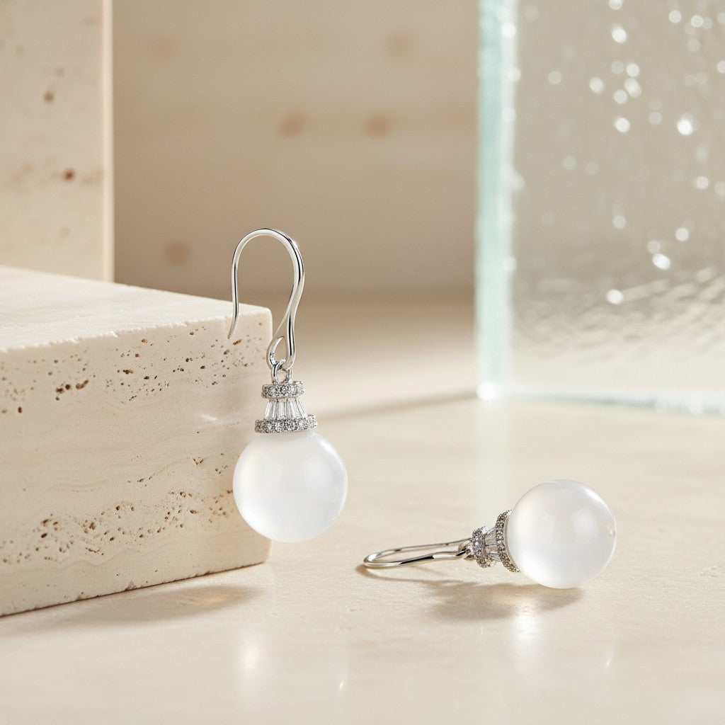 Star Crown White Chalcedony drop earrings in rhodium-plated 925 sterling silver displayed on a warm neutral stone surface