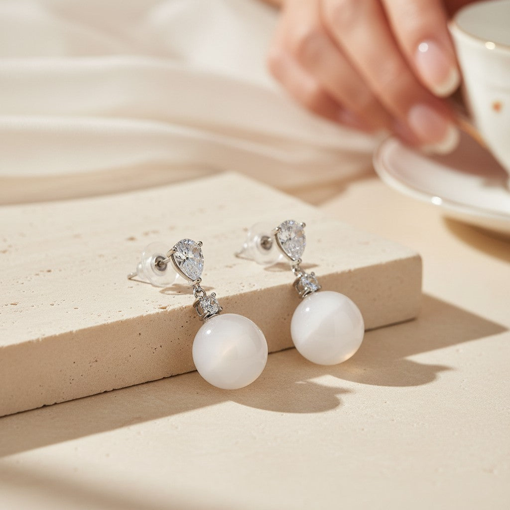 White Chalcedony drop earrings in 925 sterling silver displayed on a warm neutral stone surface